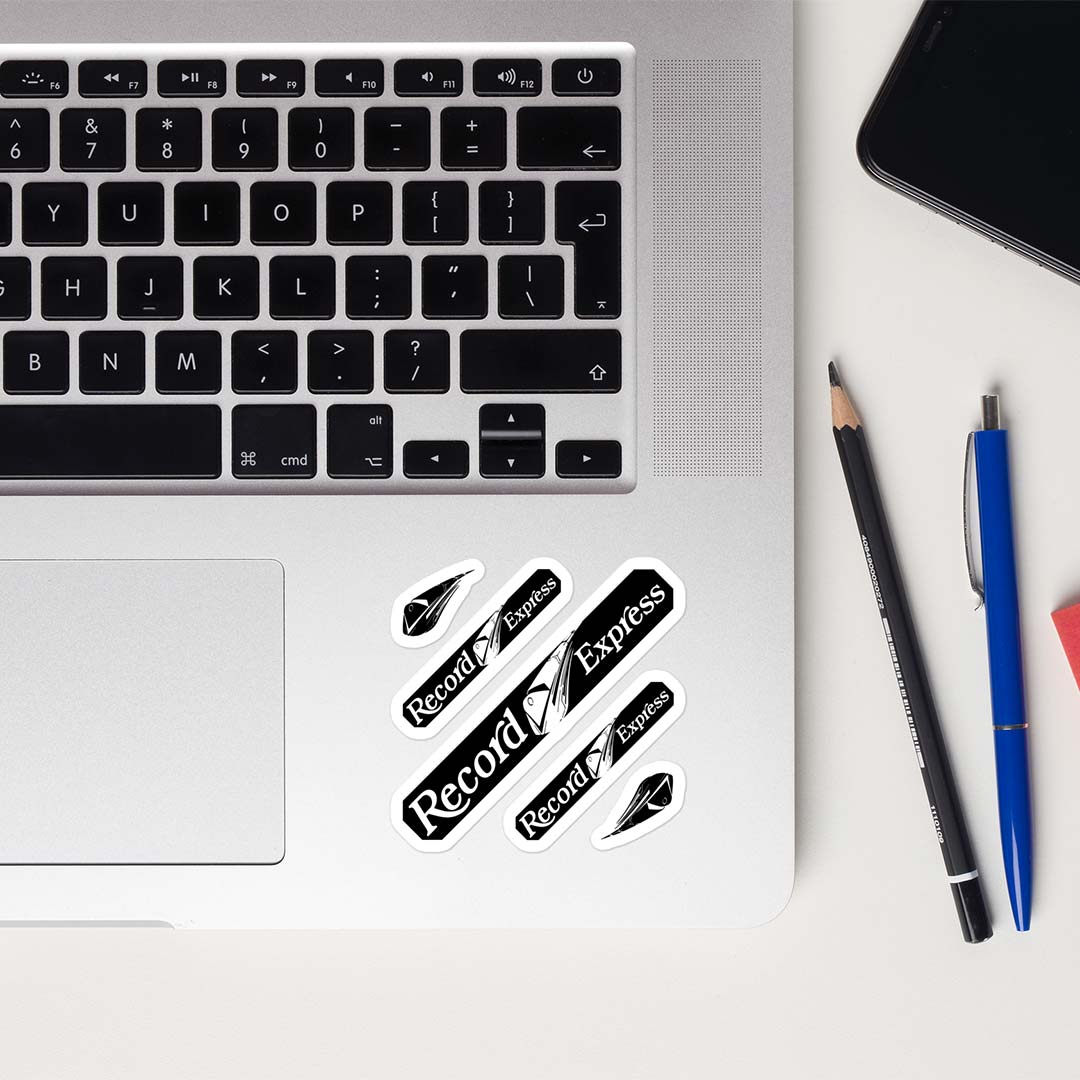 Five 'Record Express' stickers in a black and white design are shown applied to the lower left corner of a silver laptop. The scene is styled as a flat-lay on a white desk with a pencil, a blue pen, and a smartphone nearby.