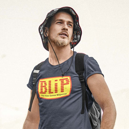 A man wearing a dark blue t-shirt with a large yellow and red 'BLIP The Video Games Magazine' logo on the chest, a patterned bucket hat, and a backpack, set against a plain off-white background.