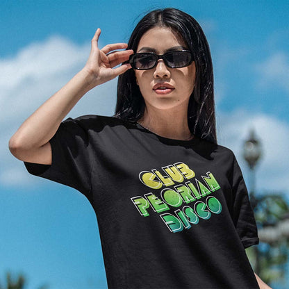 A woman wearing a black graphic t-shirt with 'CLUB PEARL DISSCO' printed in yellow, green, and blue bubble letters, photographed outdoors against a bright blue sky.