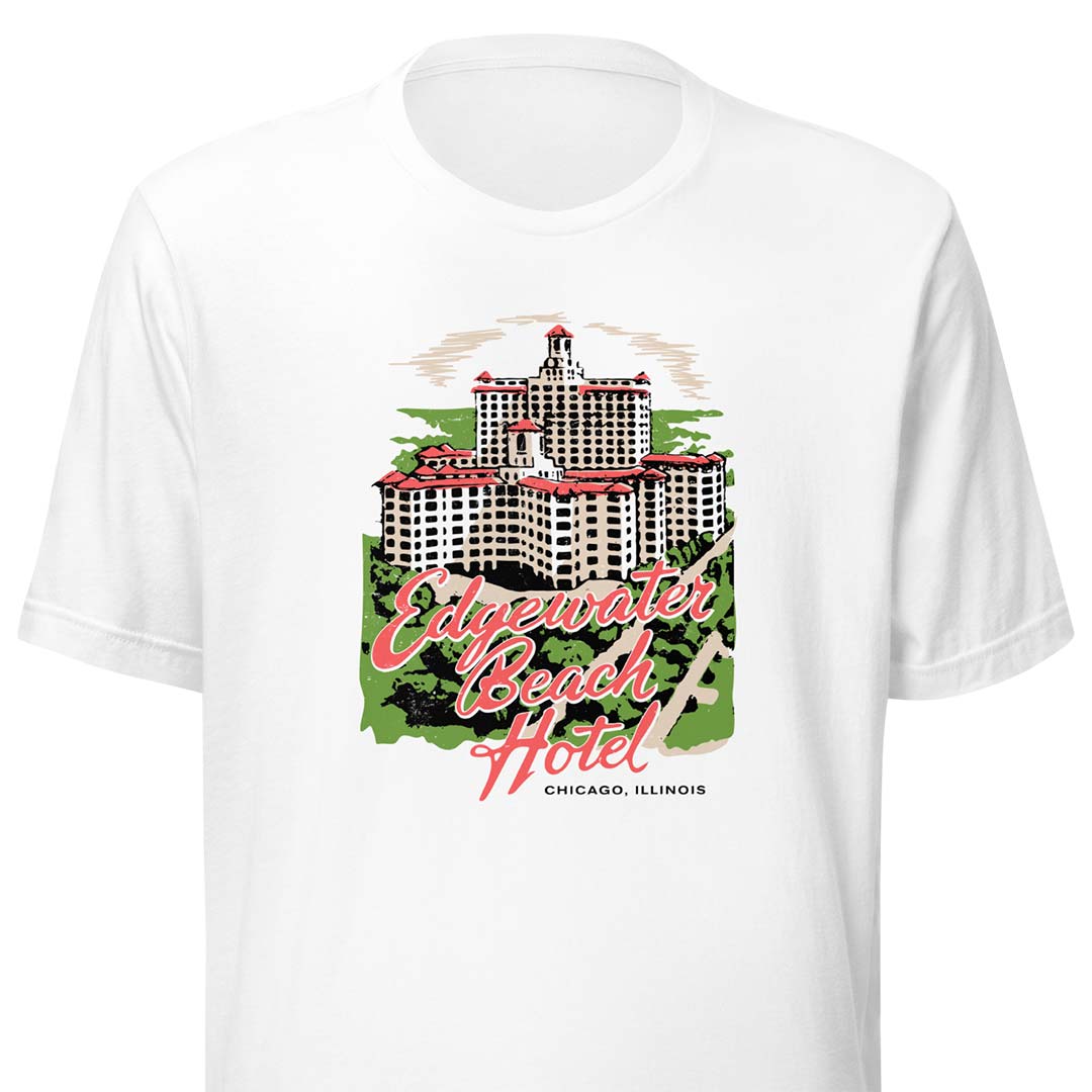 A white short-sleeve crewneck t-shirt featuring a vintage-style graphic of the Edgewater Beach Hotel in Chicago, Illinois. The graphic includes a detailed illustration of the hotel building, green trees, and pink script text reading 'Edgewater Beach Hotel' with 'CHICAGO, ILLINOIS' written below.