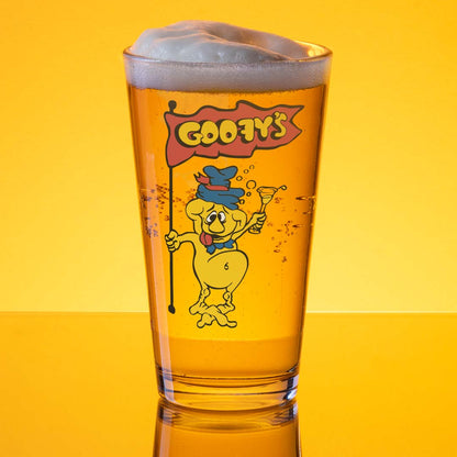 A clear pint glass filled with golden beer, topped with white foam, featuring a cartoon character and the text 'Cooby's' on the front, set against a bright yellow background.