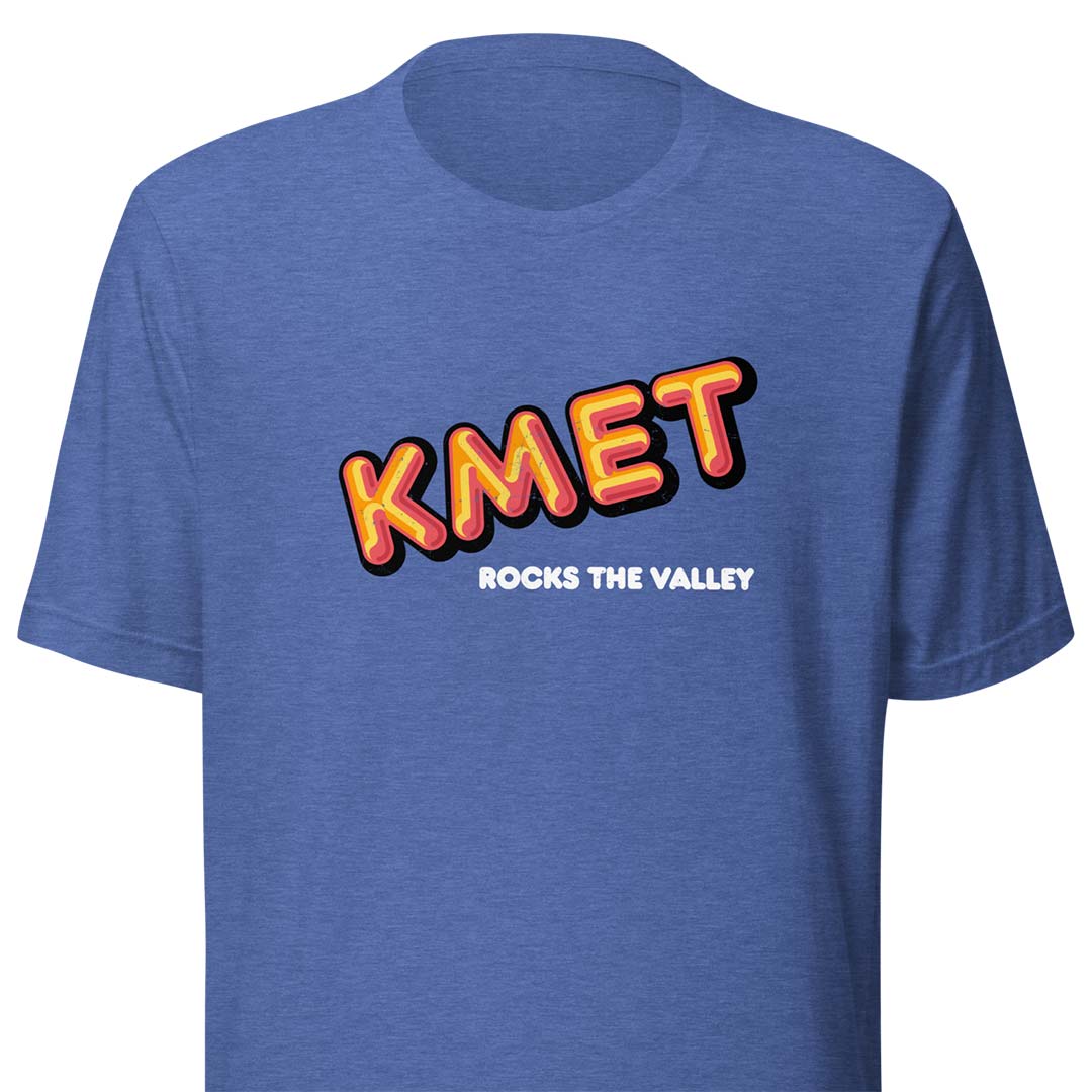 A heather blue short-sleeve t-shirt with a retro-style graphic on the chest reading 'KMET' in orange and yellow with a black outline, and the phrase 'ROCKS THE VALLEY' printed below in white.