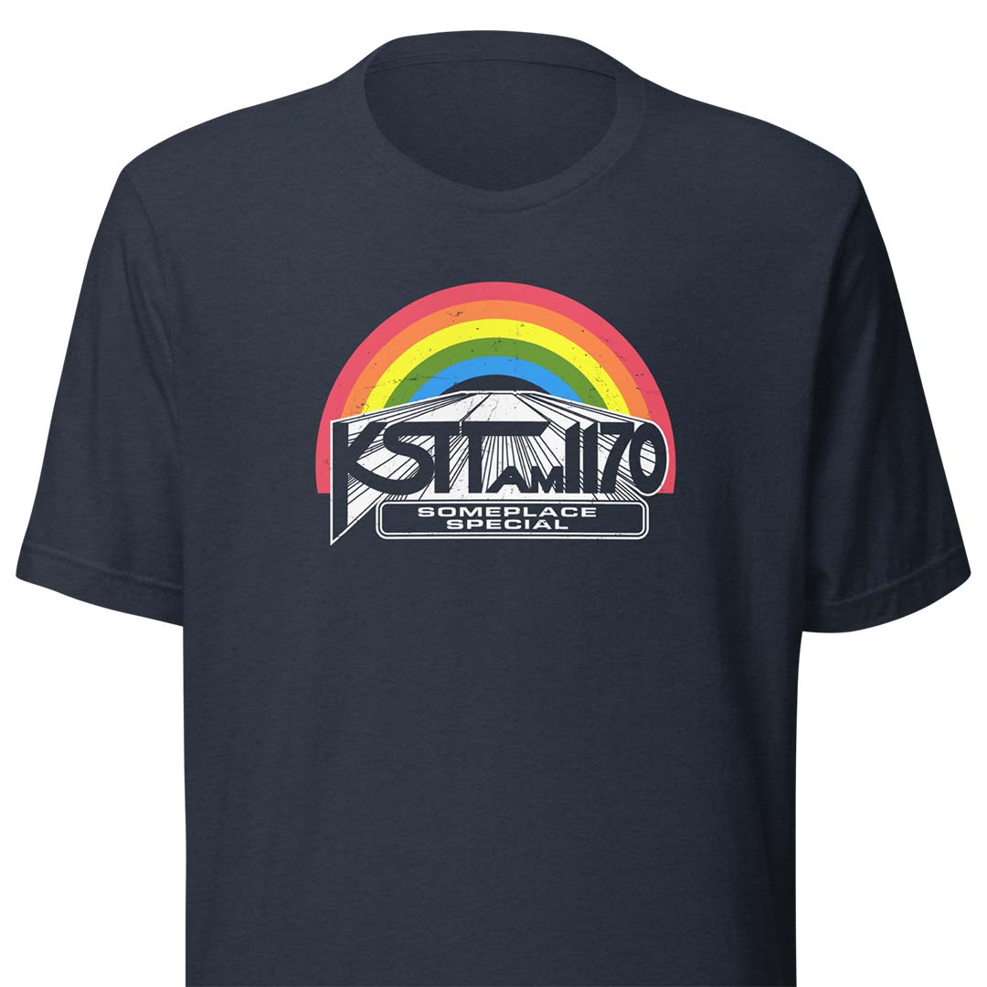 A navy blue short-sleeve t-shirt with a graphic on the chest featuring a rainbow arch over a mountain and the text 'KSTT AM 1170' and 'SOMEPLACE SPECIAL'.