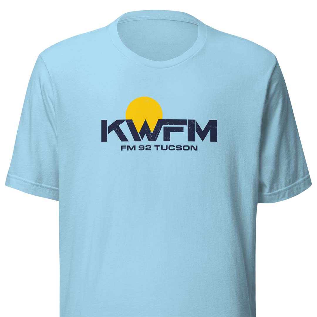 A light blue short-sleeve crewneck t-shirt featuring a yellow and navy blue 'KWFM FM 92 TUCSON' graphic printed on the chest, displayed against a solid white background.