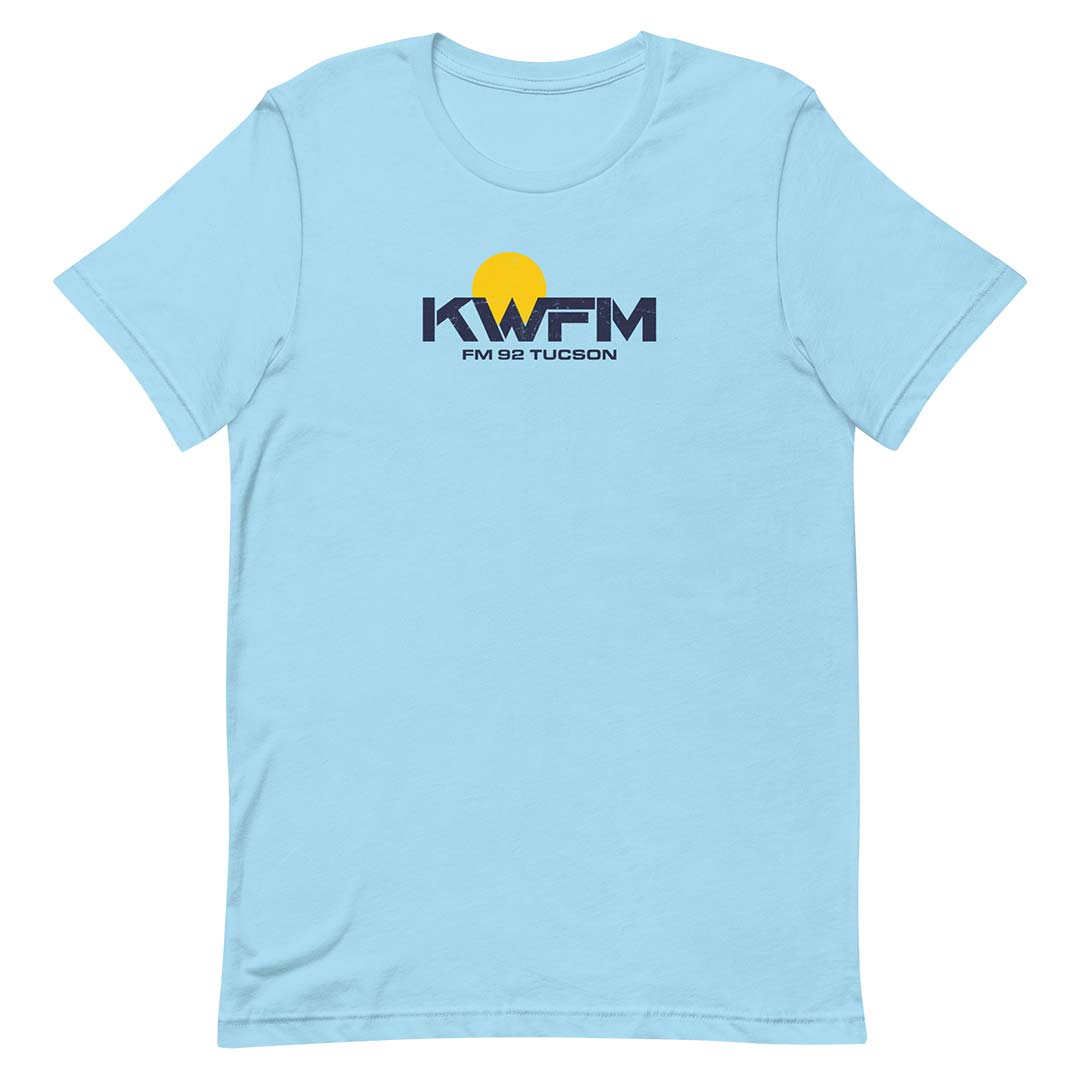 A light blue short-sleeve crewneck t-shirt featuring a 'KWFM FM 92 TUCSON' logo with a yellow sun graphic on the chest, displayed on a clean white background.