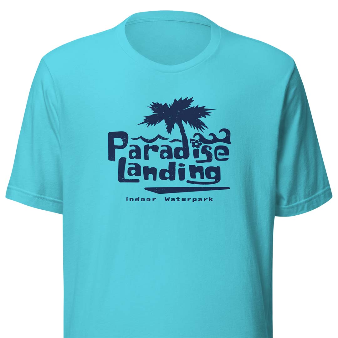 A turquoise blue short-sleeve t-shirt with a dark navy graphic on the chest featuring a palm tree and the text 'Paradise Landing' and 'Indoor Waterpark'.